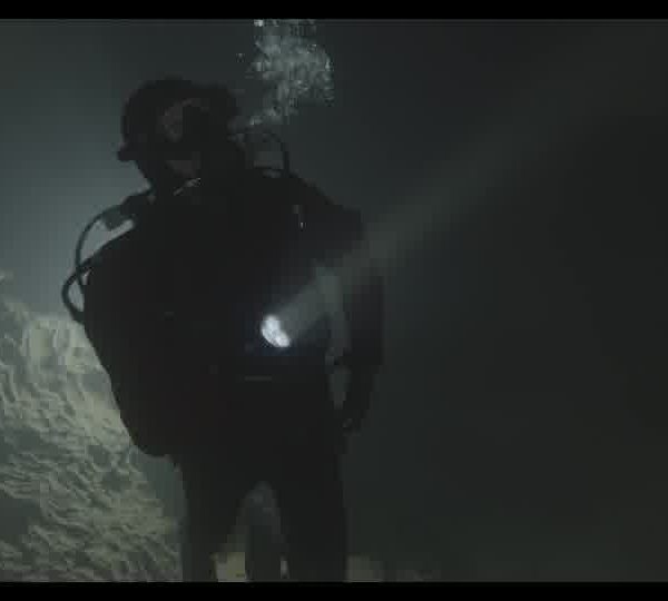 Silhouette_of_a_diver_with_a_flashlight_swimming_in_a_dark_underwater_cave_160930E7